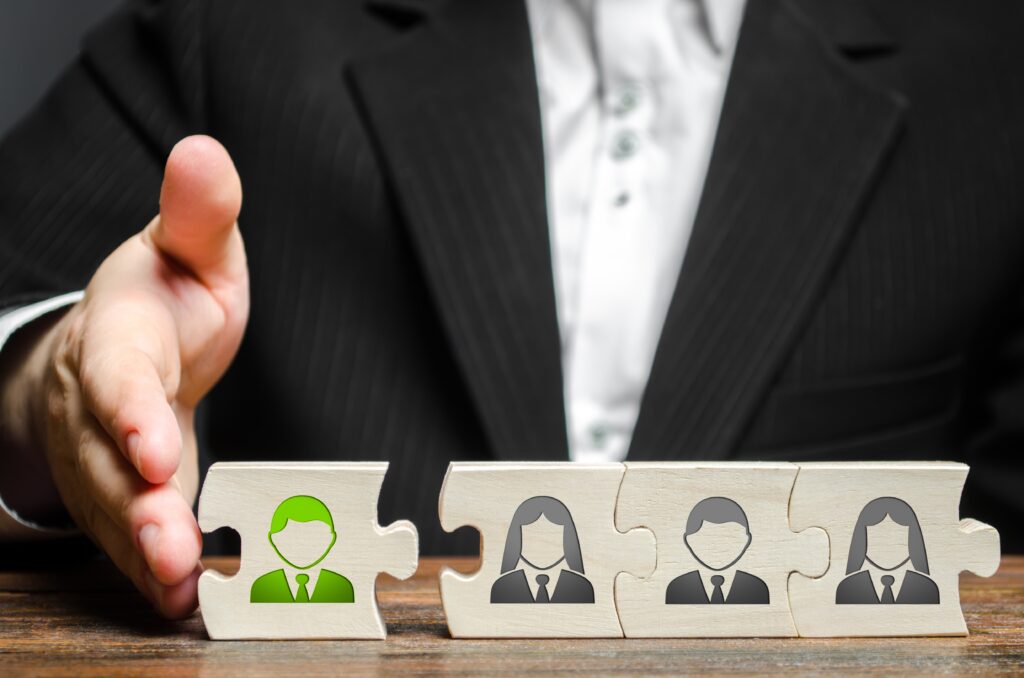 Een zakenman voegt een groen gekleurde puzzelstuk-werknemer toe aan een team, symbool voor personeelswerving en selectie.